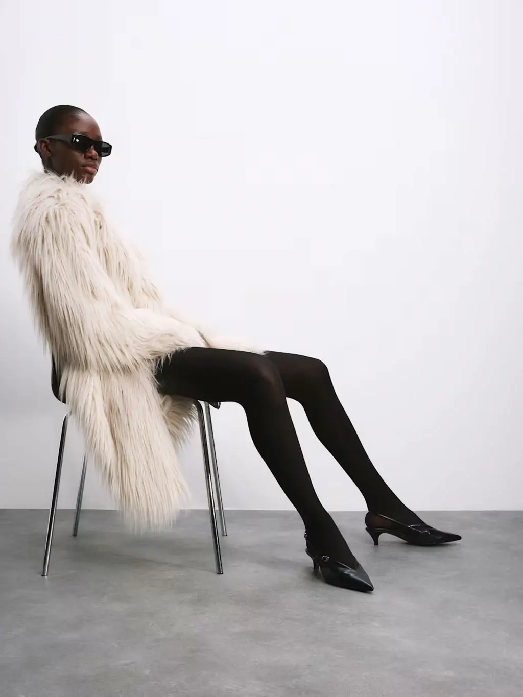 Woman wearing a white fur coat with black tights and heels