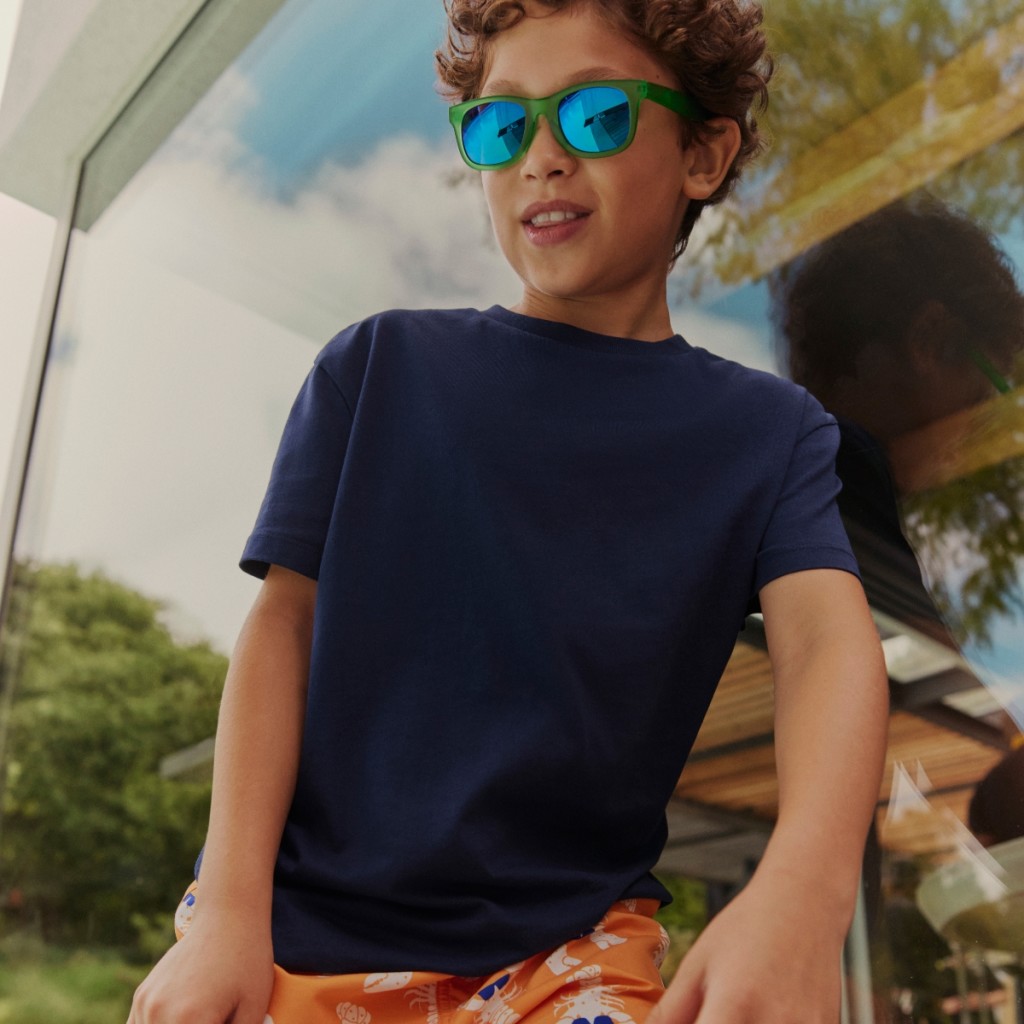 Boy wearing a navy t-shirt, patterned shorts and mirrored sunglasses. Read the kids’ holiday clothes feature