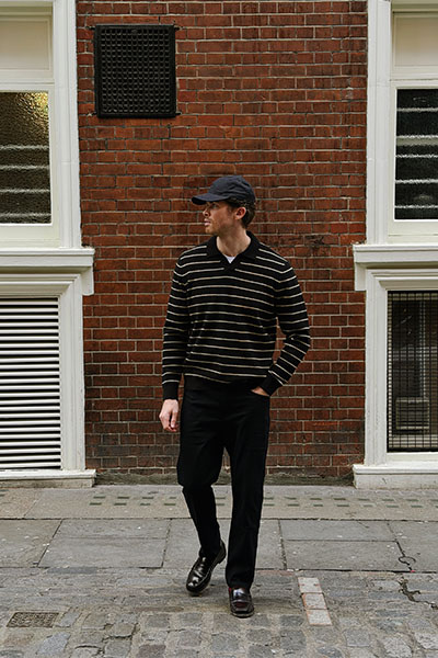 man wearing jumper, trousers and cap looking to the side