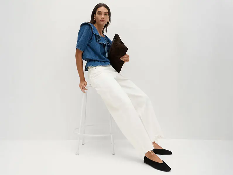 Woman wearing white wide-leg jeans with a denim blouse, black pumps and a black clutch bag