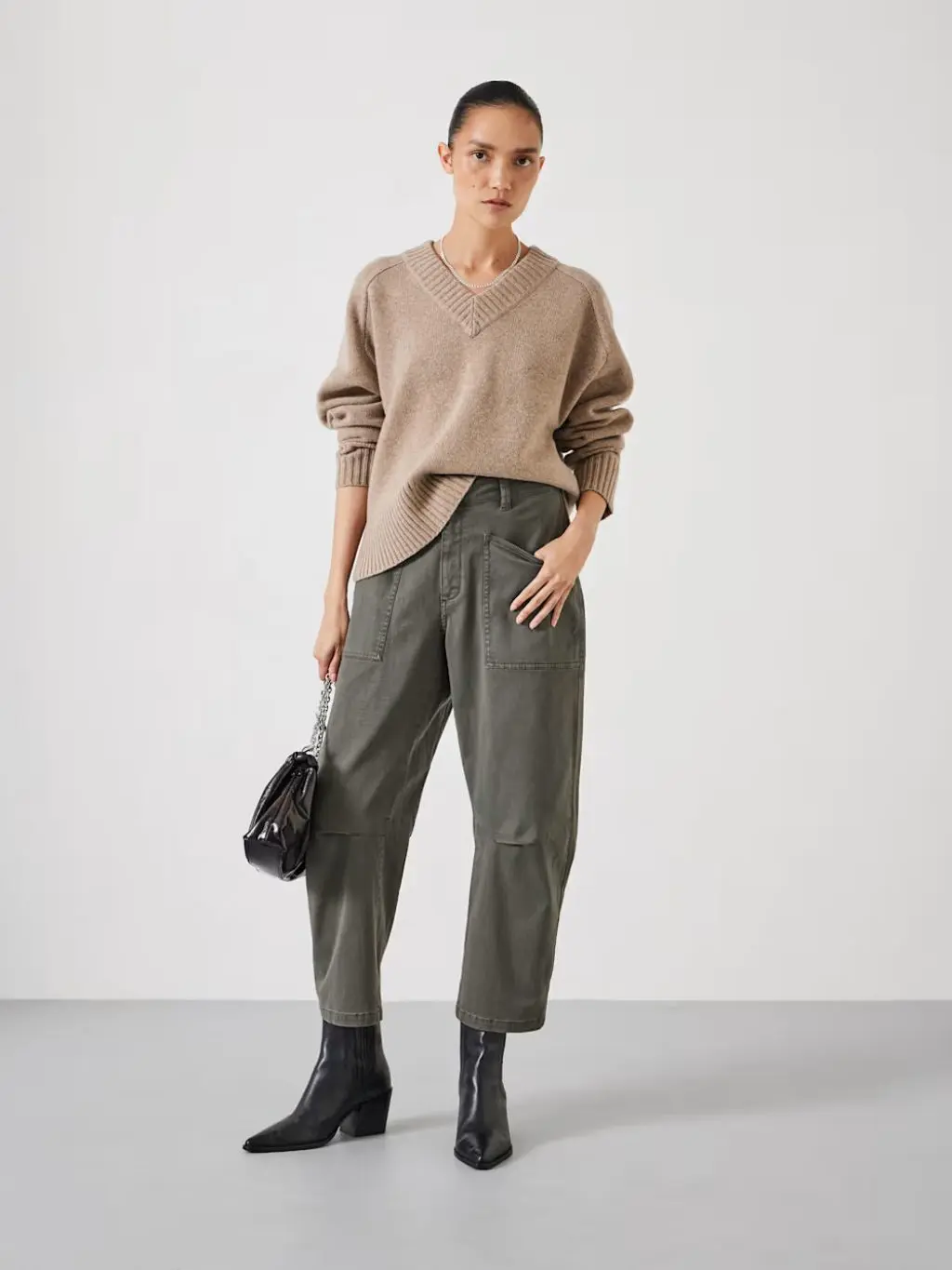 A woman wears khaki trousers with ankle boots and a v-neck jumper
