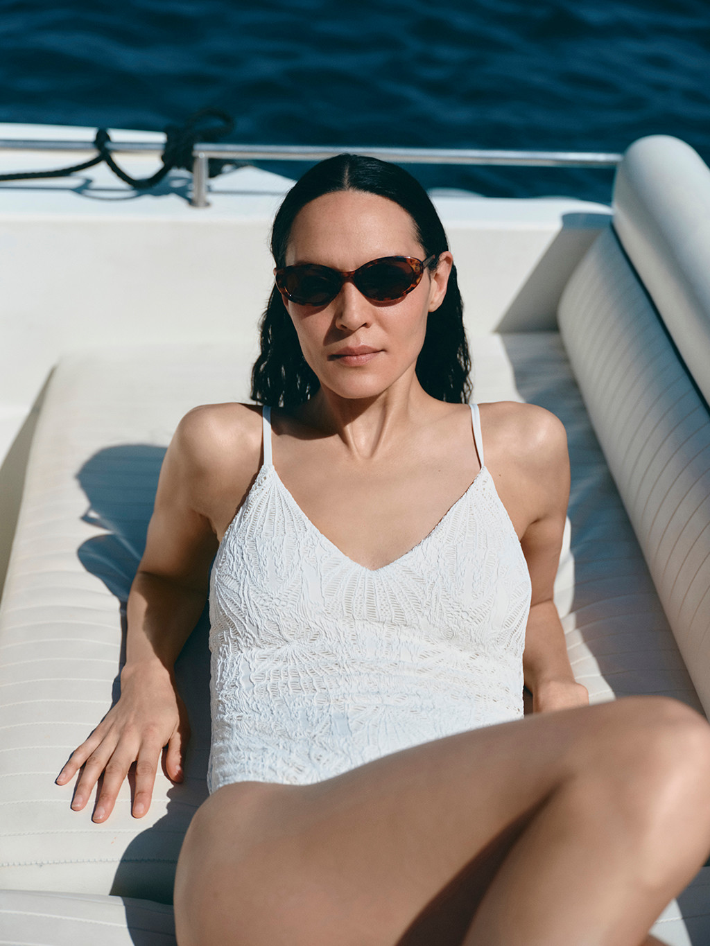 Woman wearing oval sunglasses and a white textured swimsuit on a boat