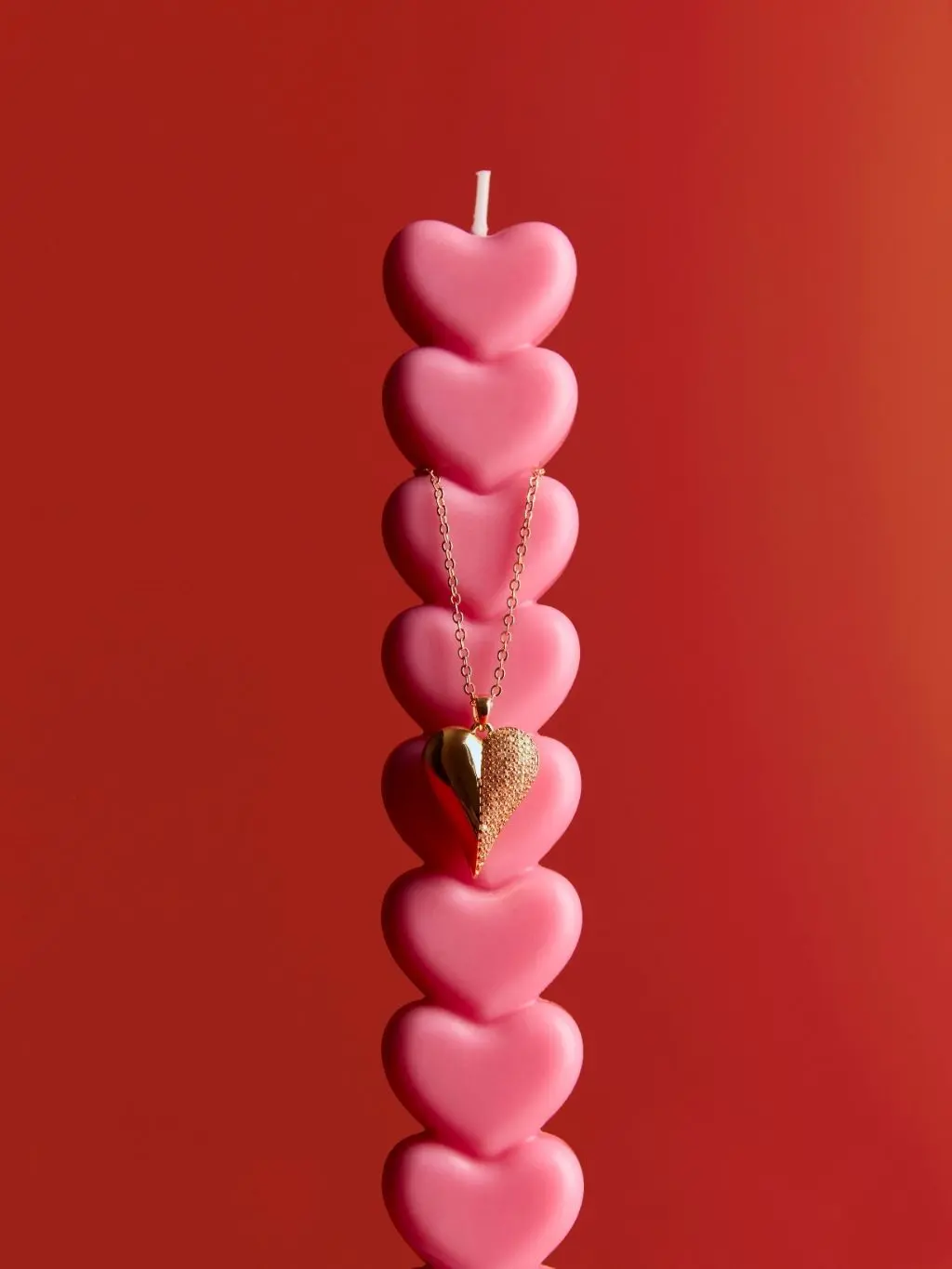 A pink heart candle with a heart necklace hanging over it, shot against a red background