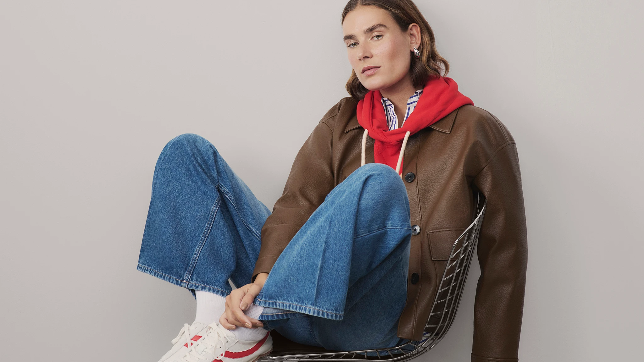 Woman wearing brown jacket, red hoodie, blue jeans and retro trainers