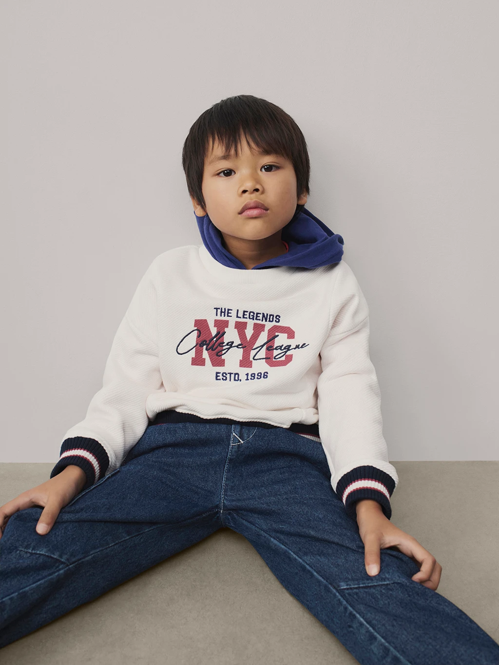Boy wearing a NYC cream sweatshirt and blue jeans