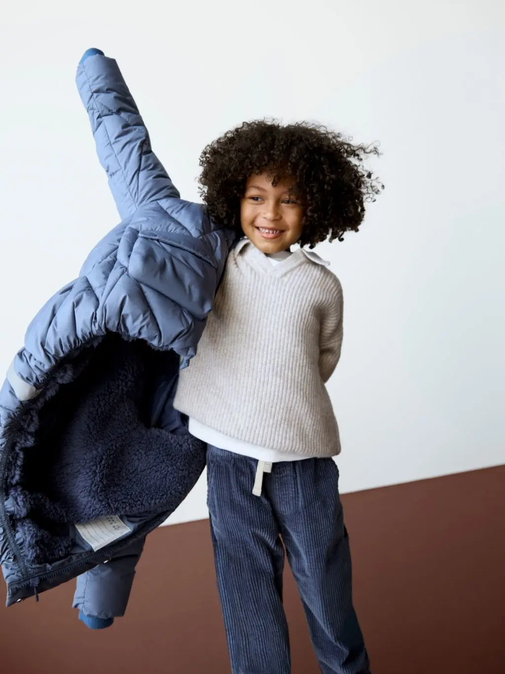 A boy putting a coat on over a jumper and thermal top