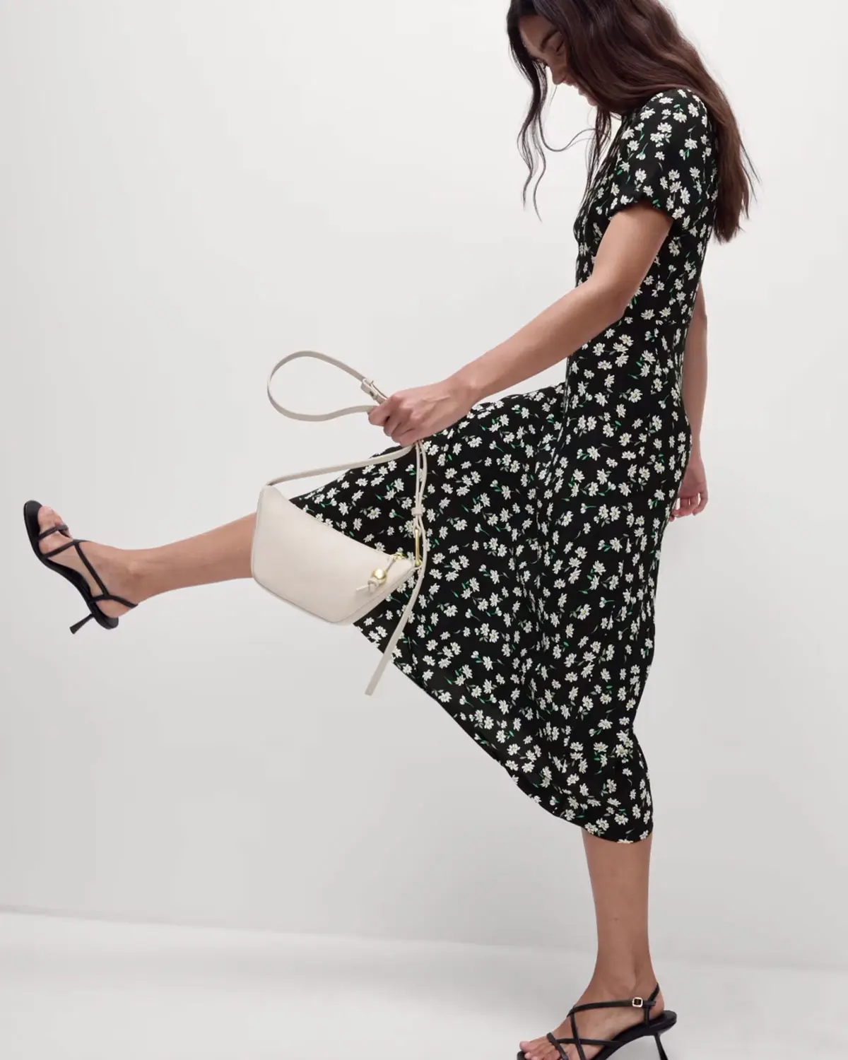 Woman wearing a black floral tea dress with black heels and a white cross-body bag