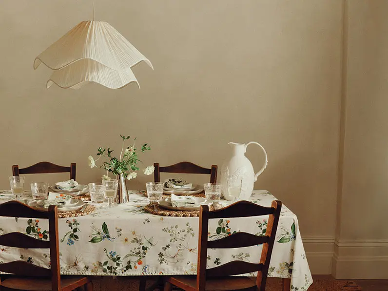 Dinner setup with a floral-printed tablecloth, raffia placemats and neutral dinnerware
