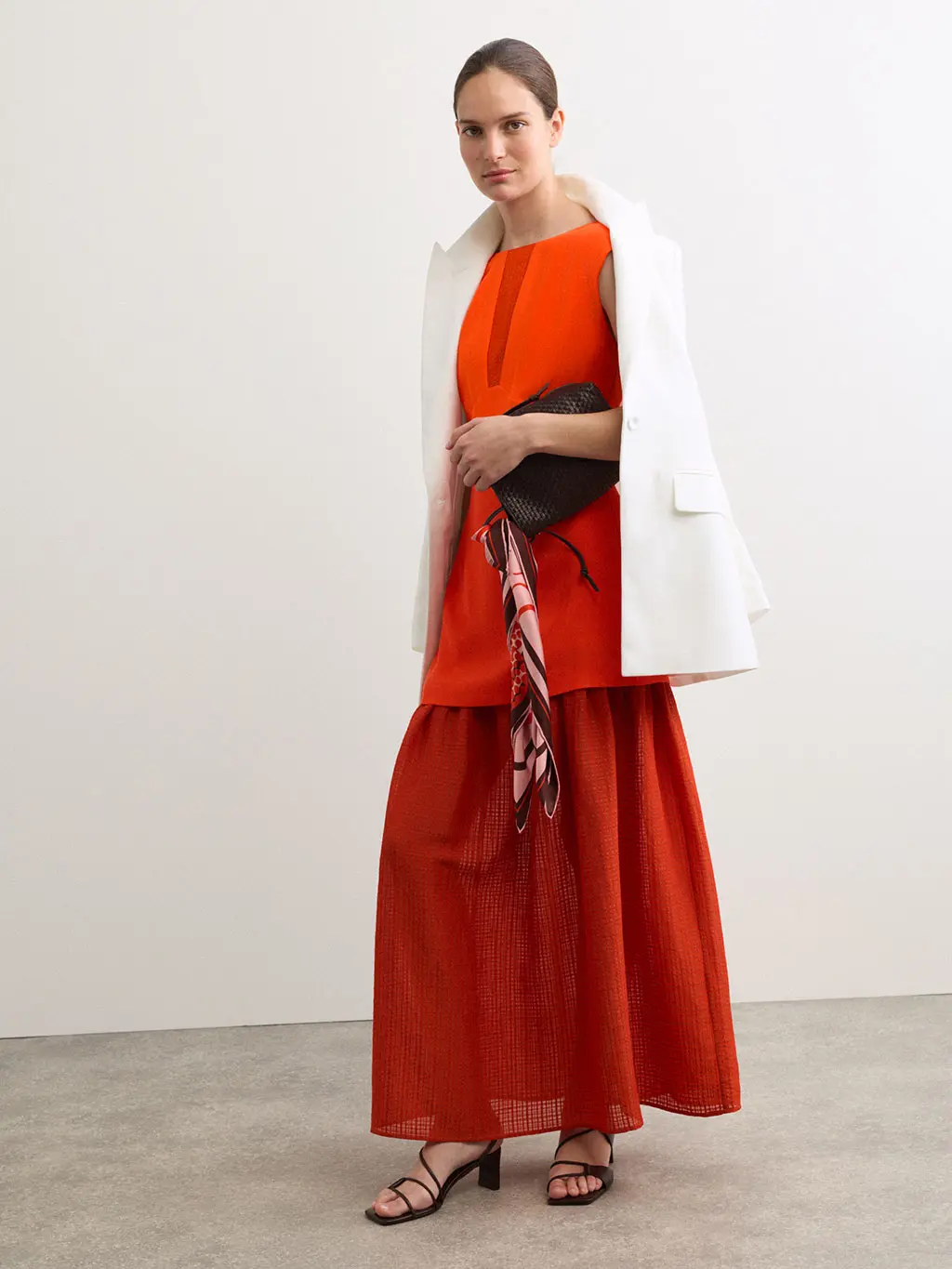 Woman wearing a red top and skirt with an ivory basketweave jacket and heels