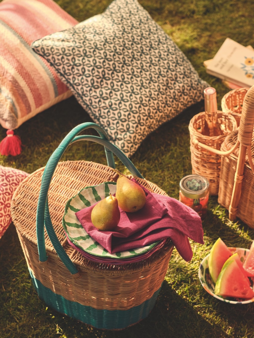 Picnic basket surrounded by patterned cushions. Shop garden accessories