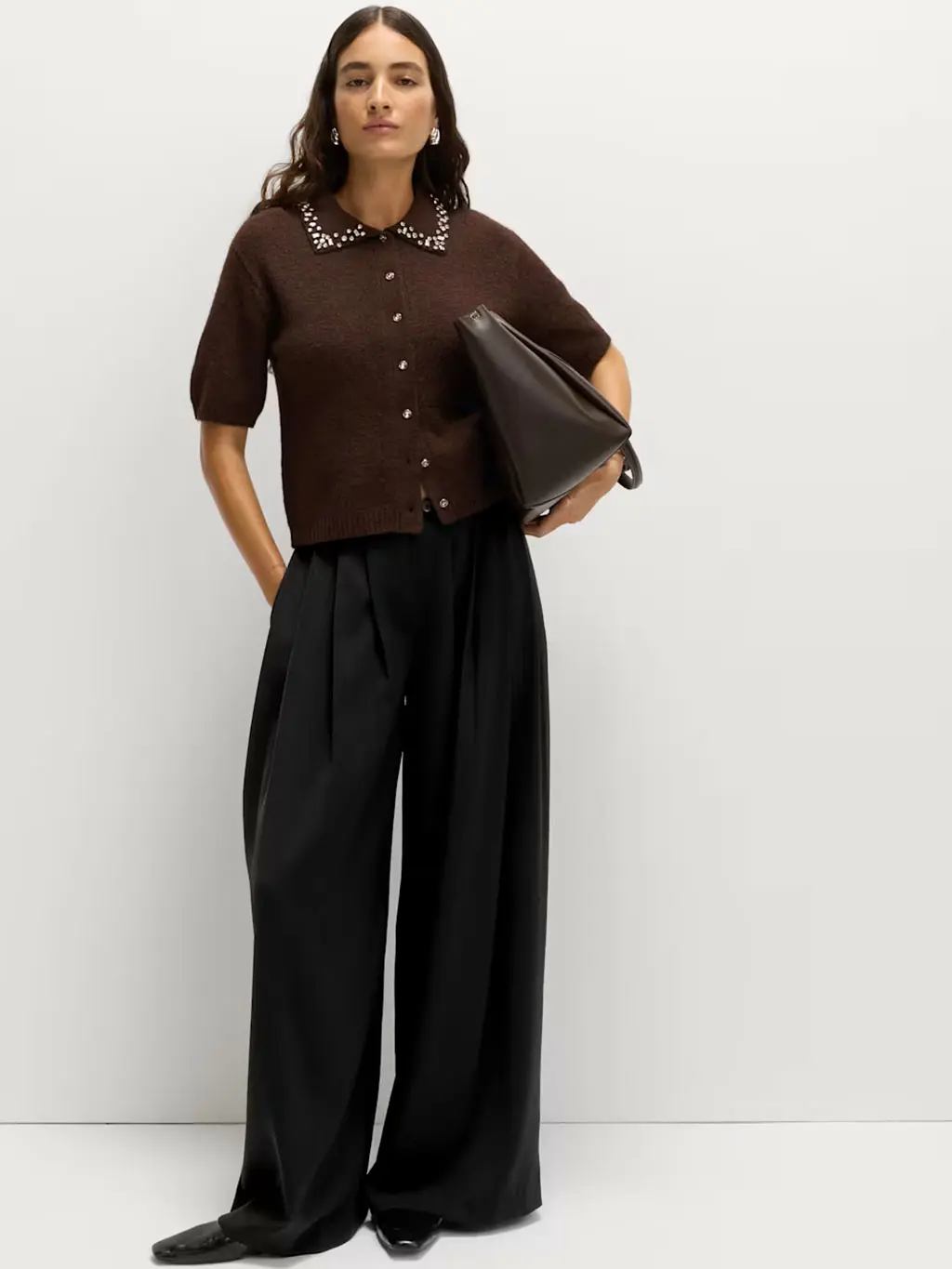 Woman wearing black trousers with an embellished brown cardigan, black pumps and a brown tote bag