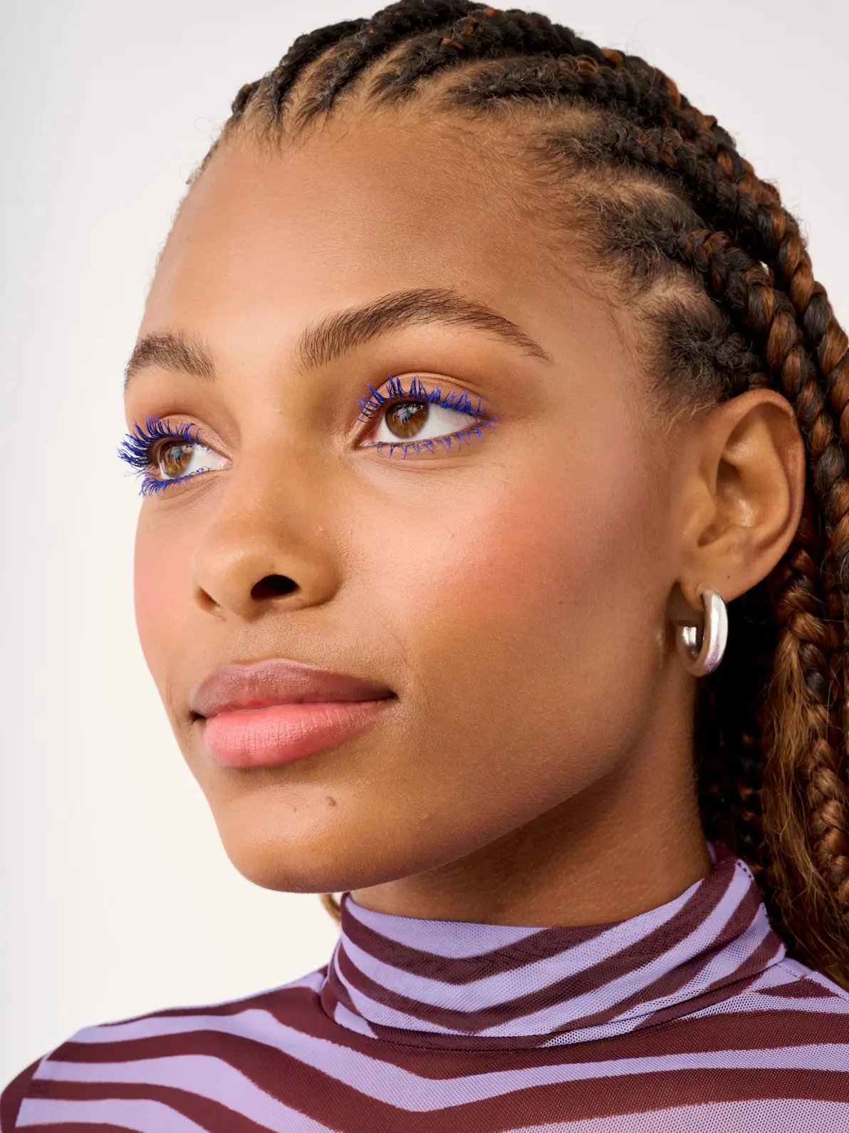 Woman wearing blue mascara and striped purple and red high-neck top