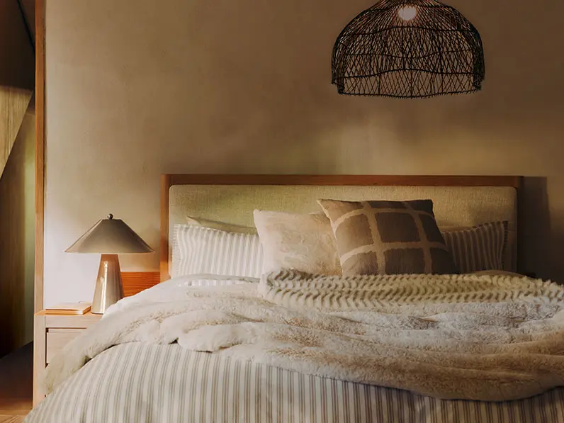 Neutral bedroom with green and white striped bedding and cosy faux fur throw.
