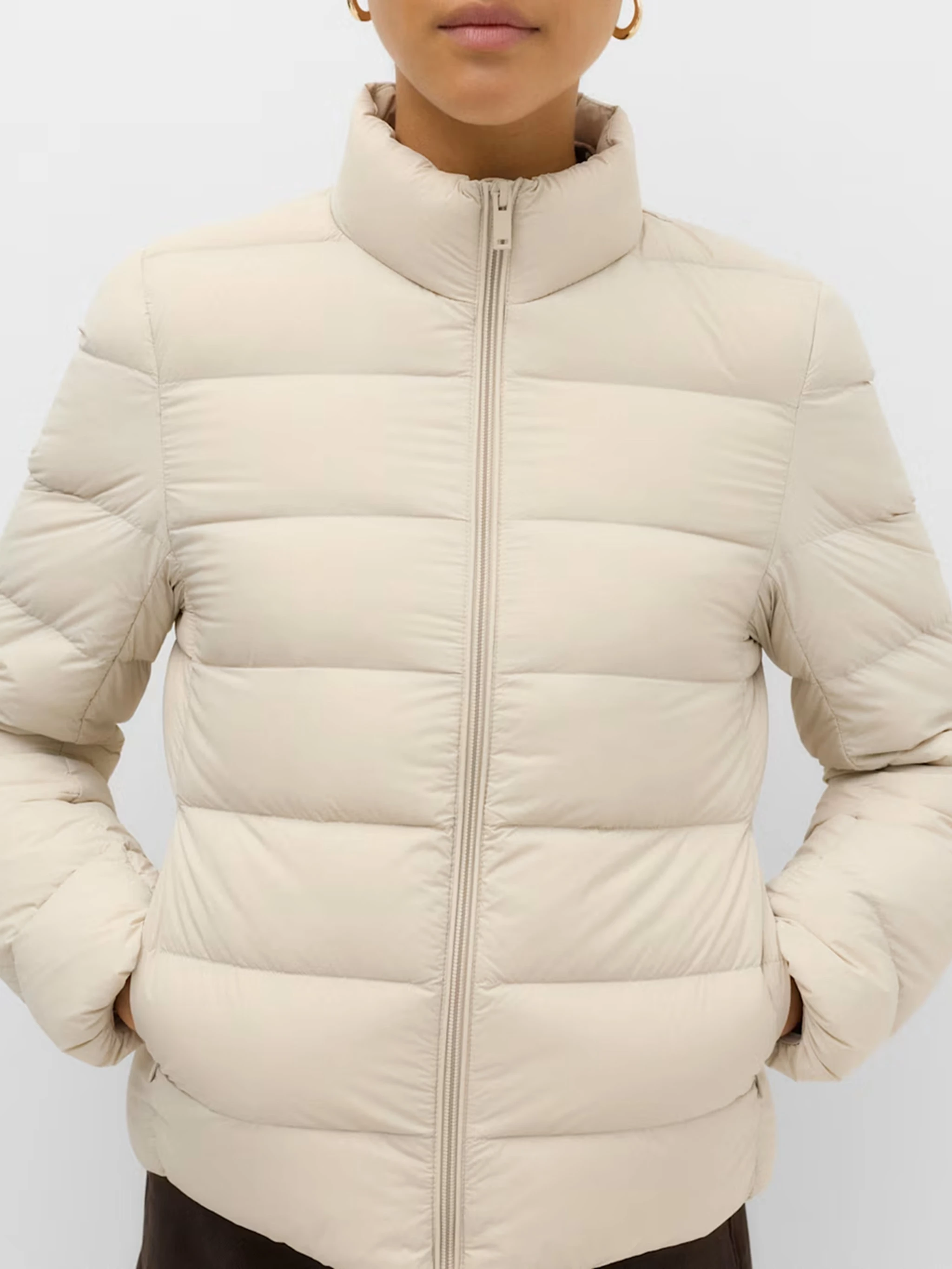 Close up of a model wearing cream puffer jacket with a high neck and padded finish.