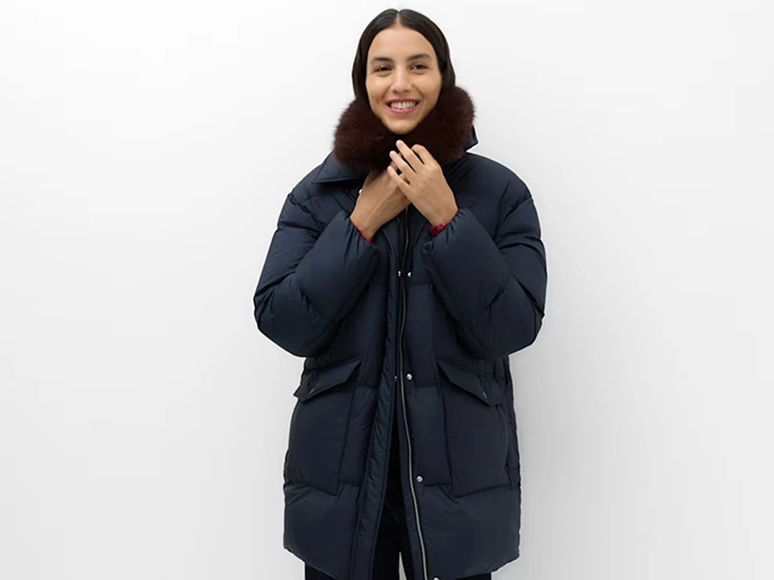 Woman wearing a navy blue long puffer coat with a faux fur collar.