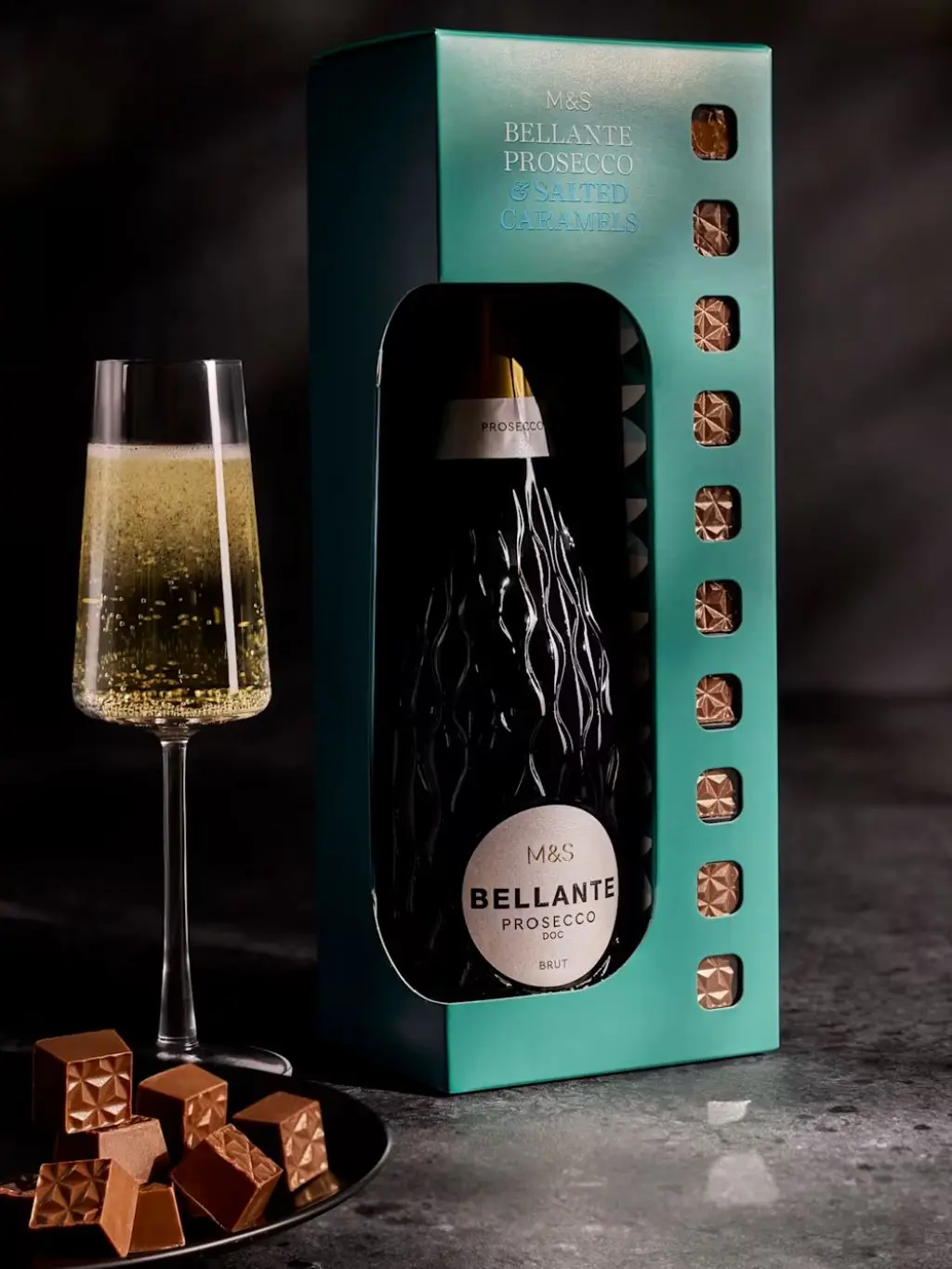A bottle of prosecco in a box with a flute of champagne and chocolates