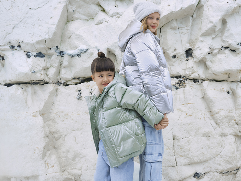 Girls wearing pastel padded rain coats by beach cliffs