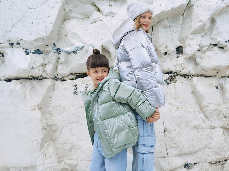 Girls wearing pastel padded rain coats by beach cliffs