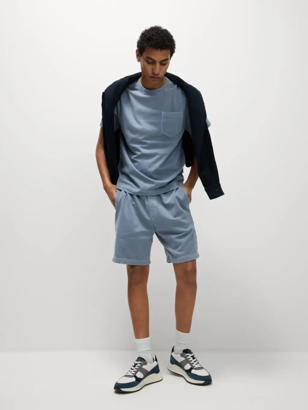 A man wears a matching T-shirt and jersey shorts with a sweatshirt over his shoulders and trainers