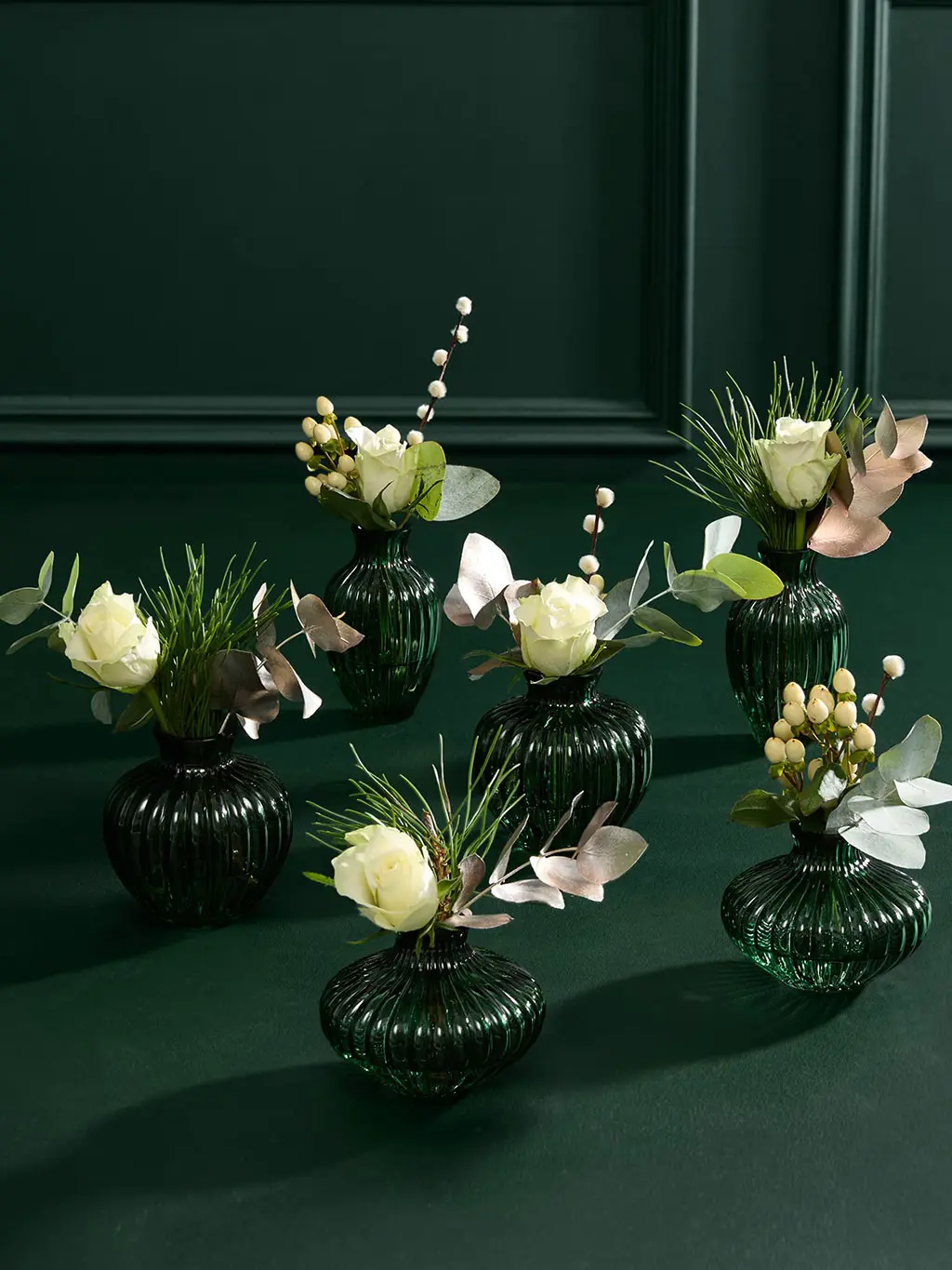 Cluster of green glass vases with sprigs of greener and white roses.