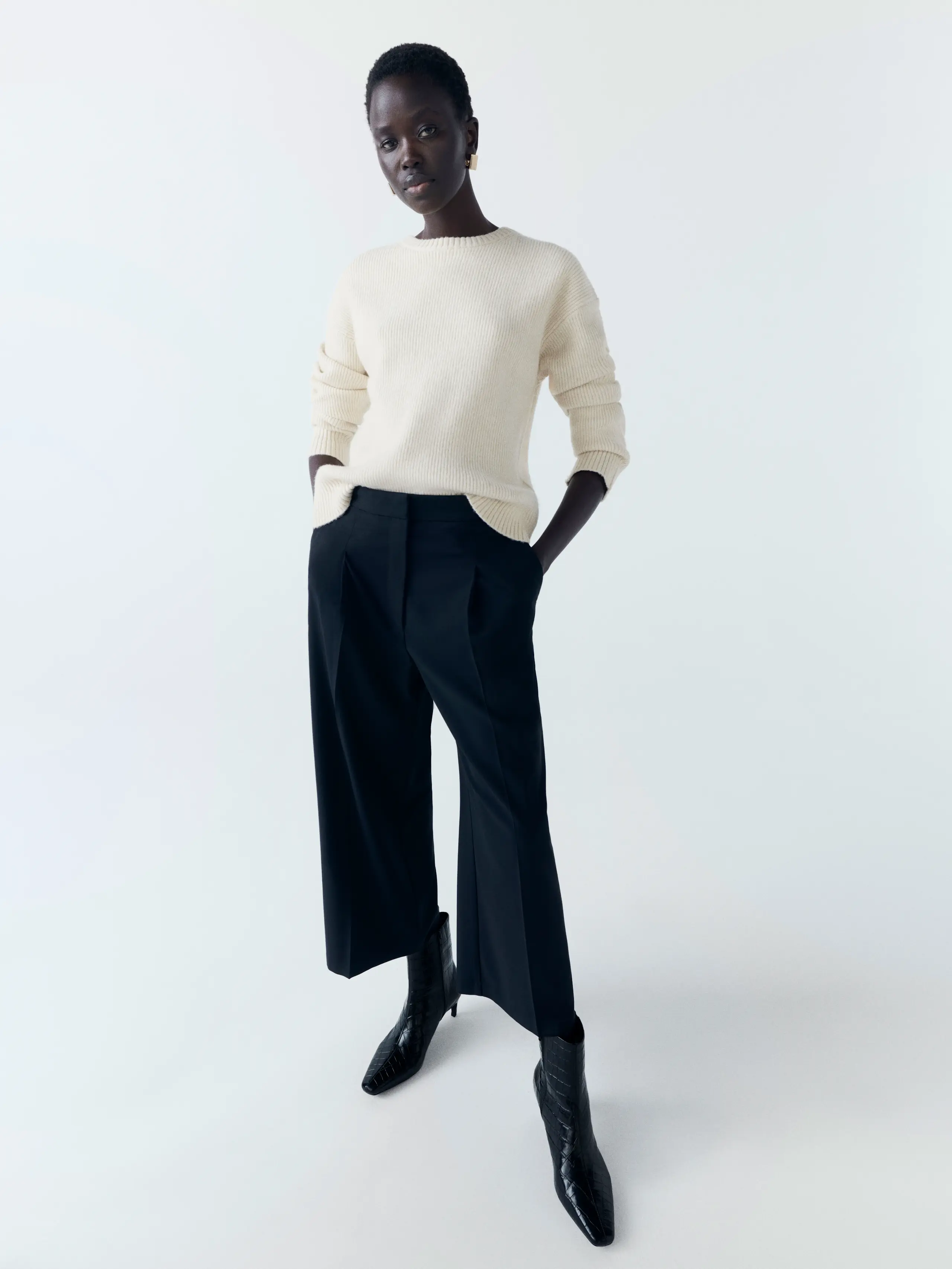 Woman wearing white jumper, black smart trousers and black heeled ankle boots