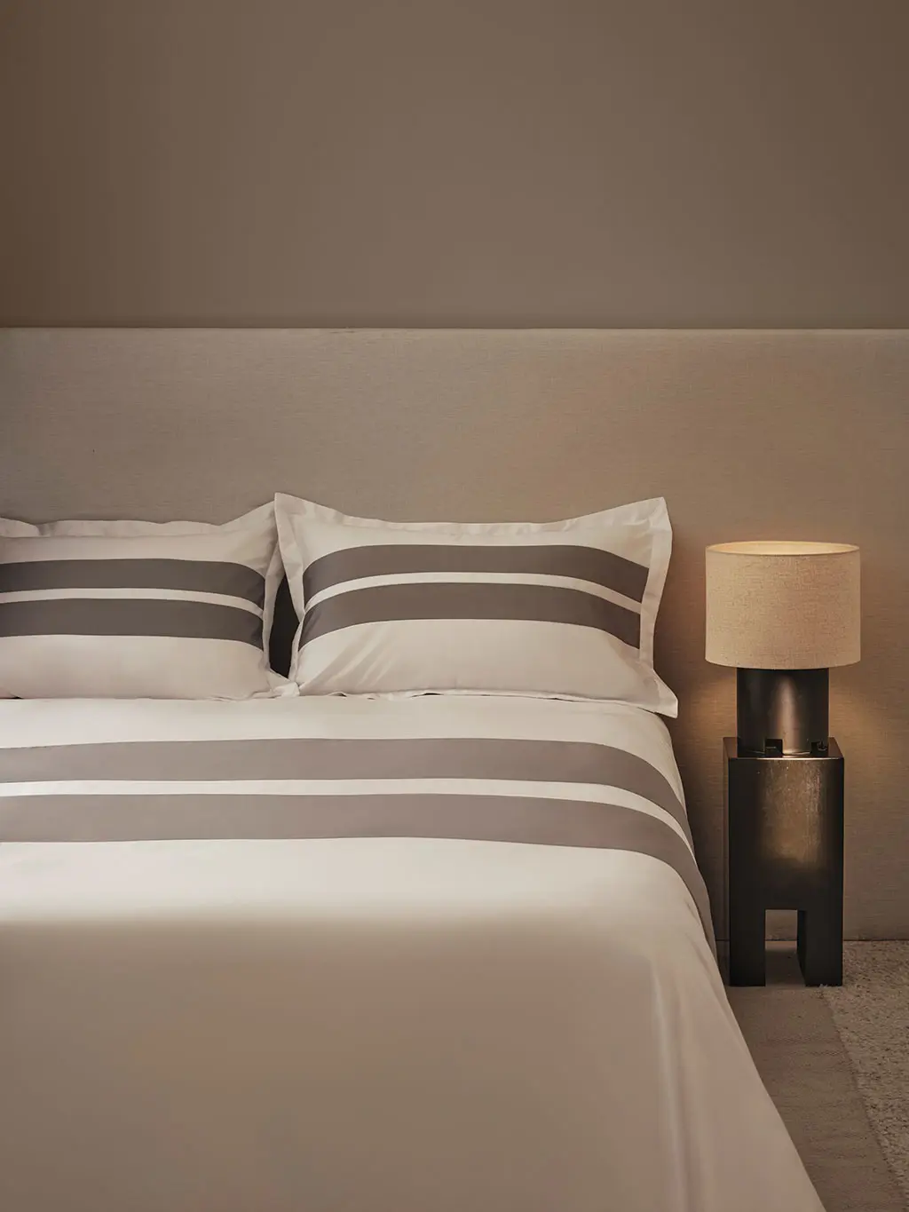 Neutral bedroom setting with white bedding and a bedside light.