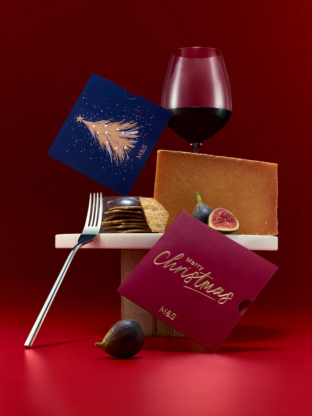 Group of cheese, crackers and M&S gift cards in front of a glass of red wine.
