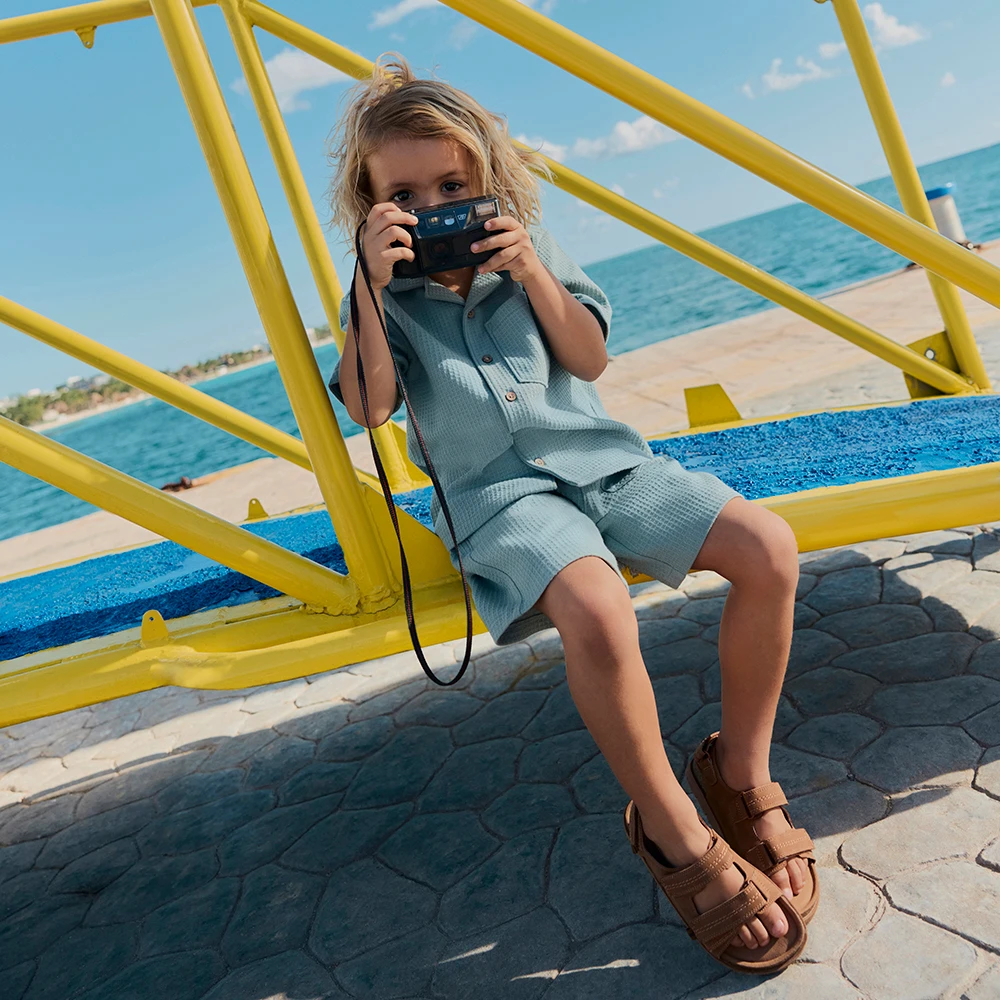 A boy wears a light blue co-ord and brown sandals on holiday