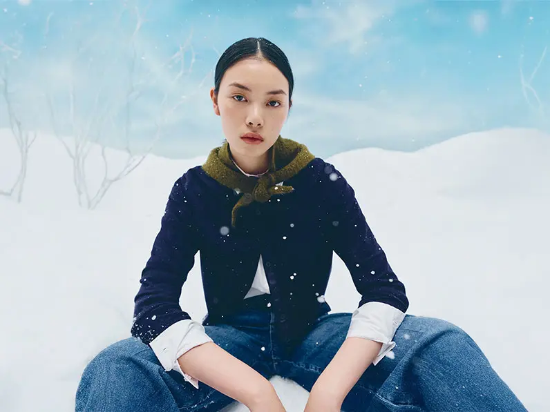 Woman wearing a blue cardigan, white shirt, blue jeans and a green scarf