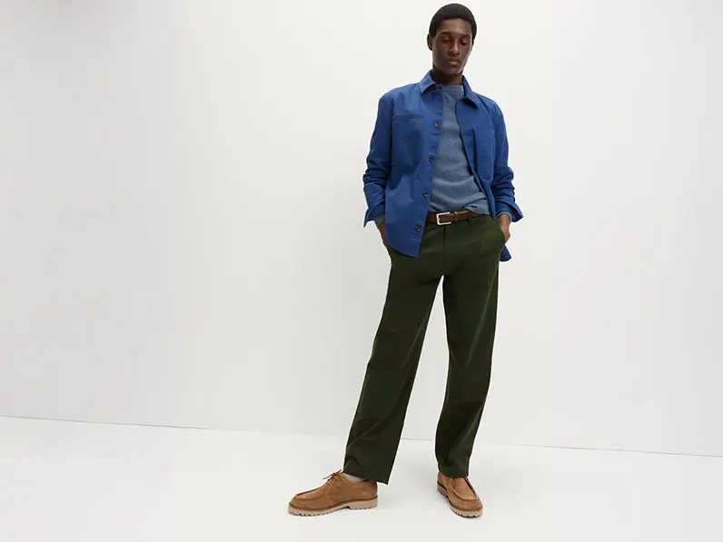 Man wearing green chinos with a blue sweater, navy overshirt and brown suede boots
