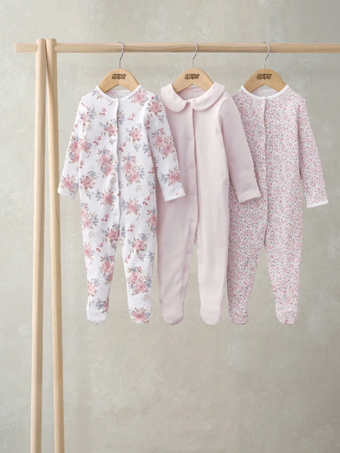 Three sleepsuits hanging on rail in pink and floral prints