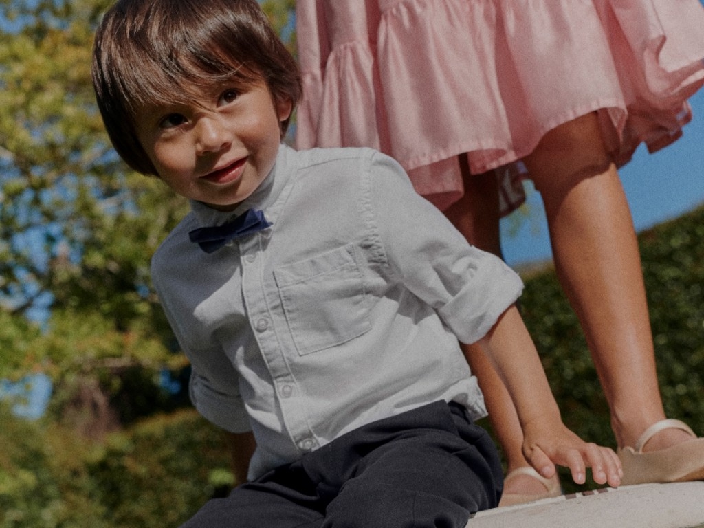 Boy wearing a white short-sleeved shirt with a dark blue bowtie and black trousers. Shop boys occasionwear