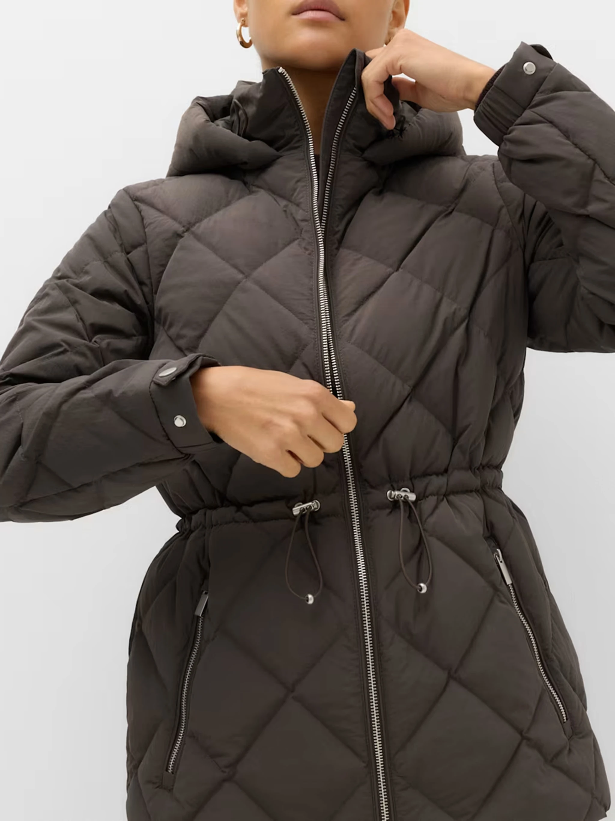 Close up of a woman wearing a brown quilted jacket with a cinched waist and silver zip down the front.