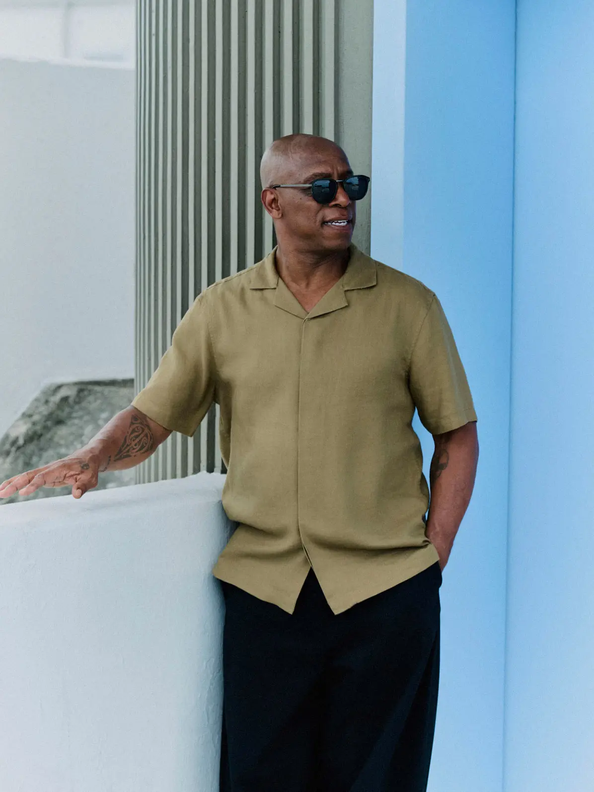 Man wearing green shirt with black trousers and sunglasses 