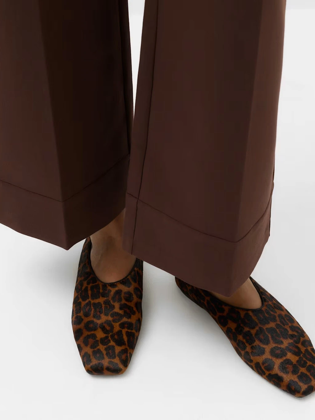 Close up of a model wearing brown wide leg smart trousers and leopard print ballet flats.