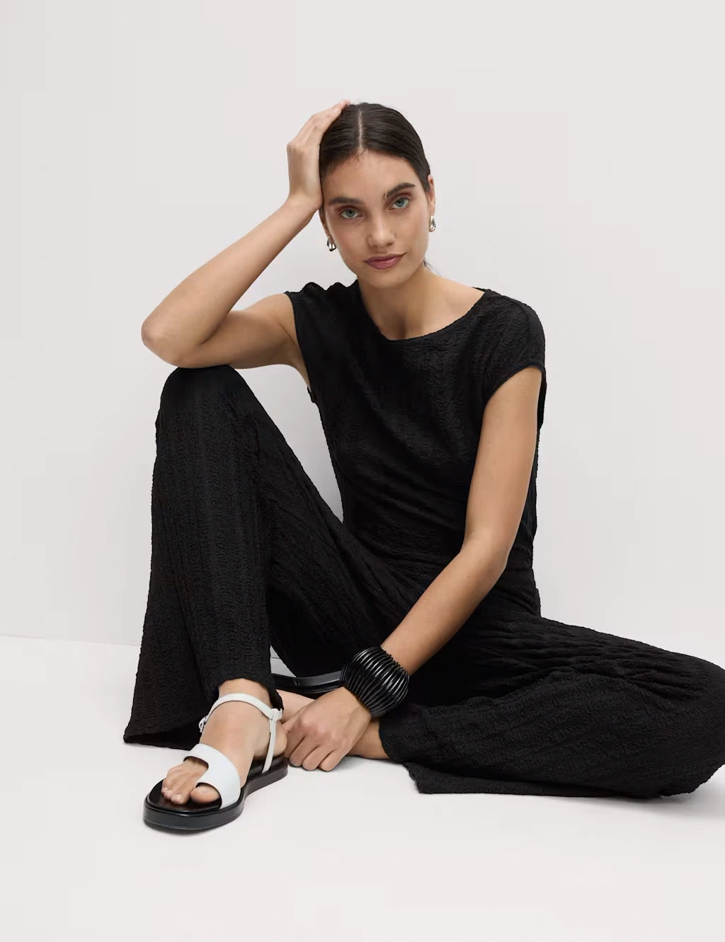 Woman wearing a black T-shirt, black trousers with white and black sandals.