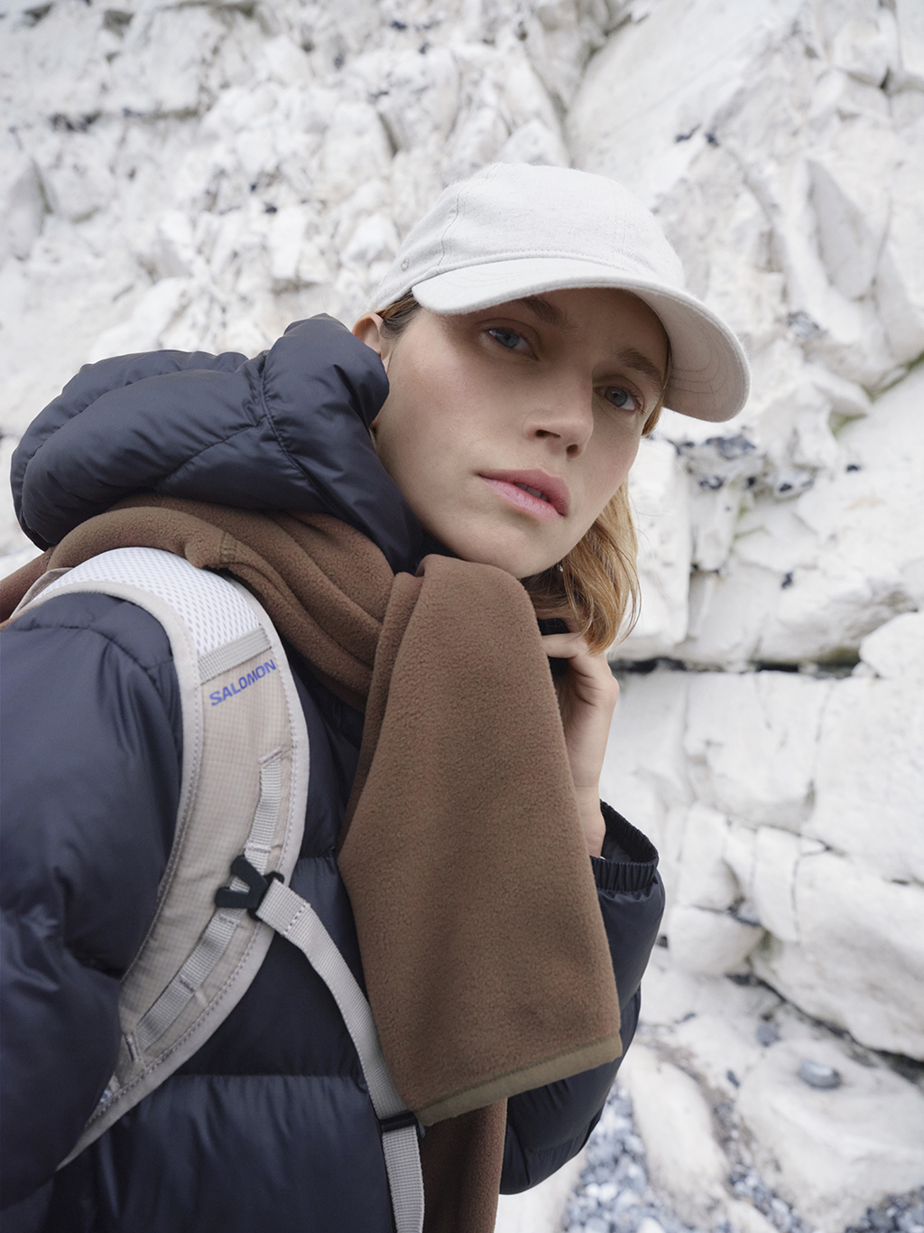 Woman wearing puffer jacket, scarf, backpack and baseball hat