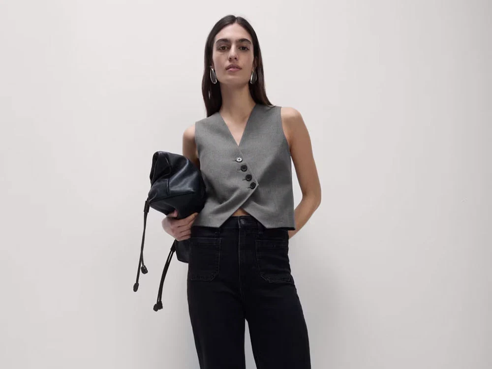 Woman wearing grey waistcoat, black jeans and black bag