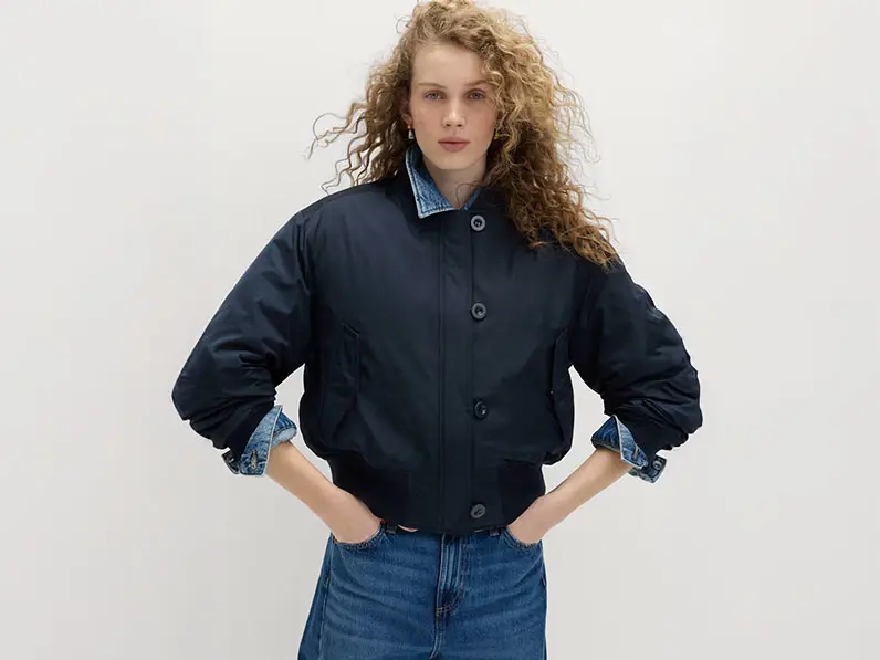 Woman wearing a navy bomber jacket over a denim shirt with jeans