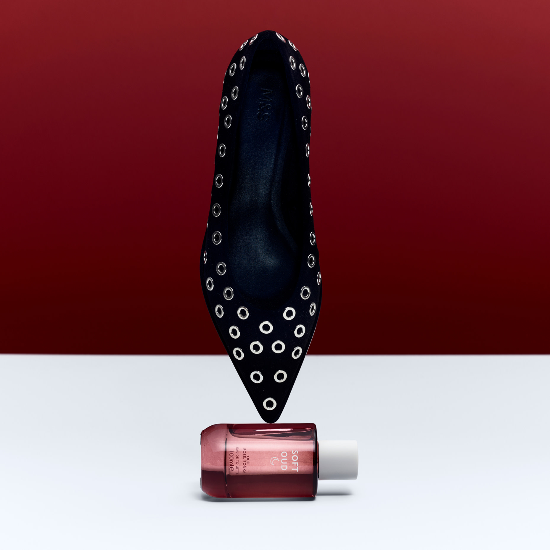 Pointed black ballet flat shoe balanced upon a Soft Oud perfume bottle