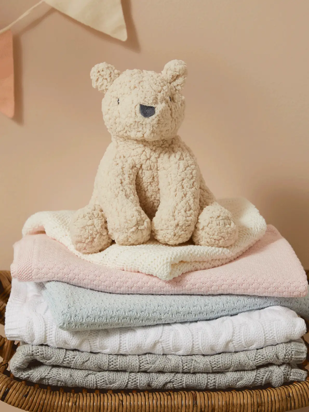 Gif of hanging mobile of soft animal toys, a teddy bear on top of baby pink, blue and cream blankets, and an assortment of soft toys
