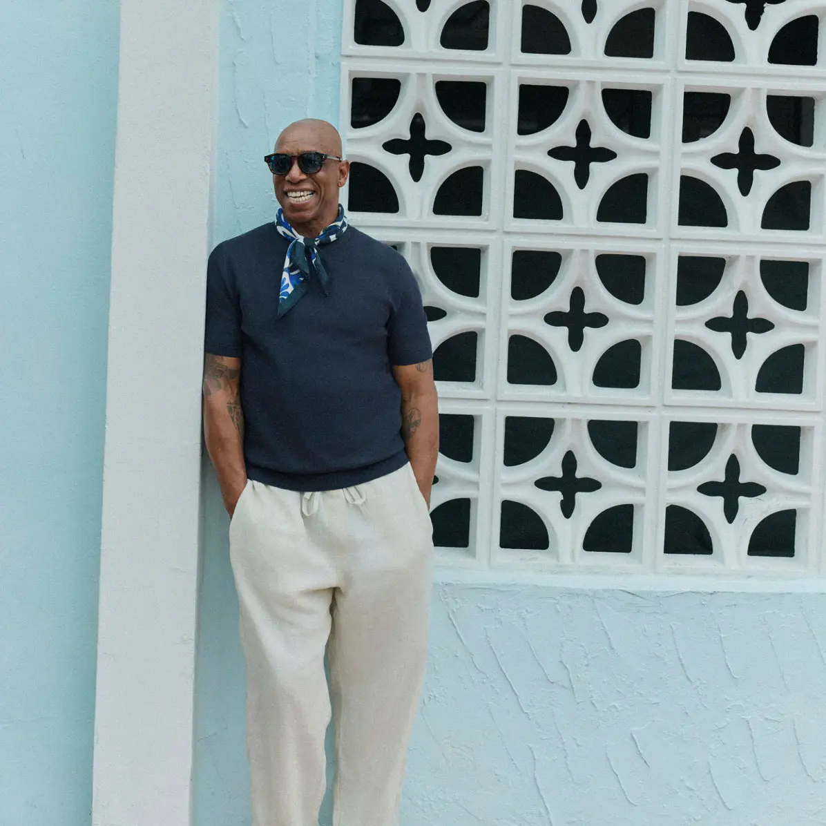 Man wearing navy knitted top with light-toned trousers, patterned neck scarf and sunglasses