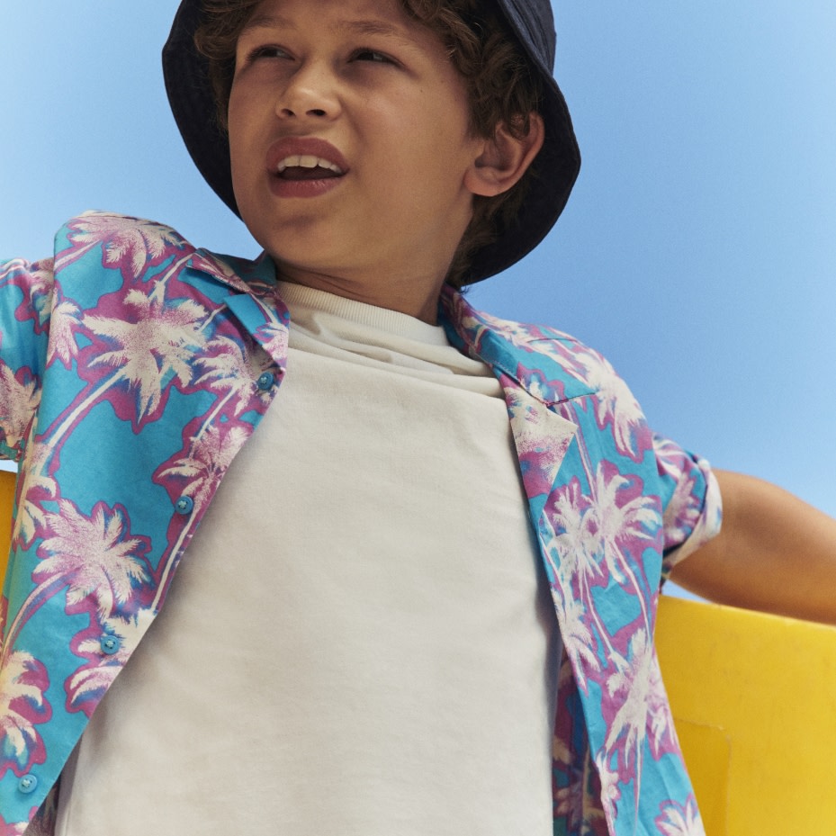 Boy wearing a blue floral shirt and white T-shirt. Shop boys’ clothing