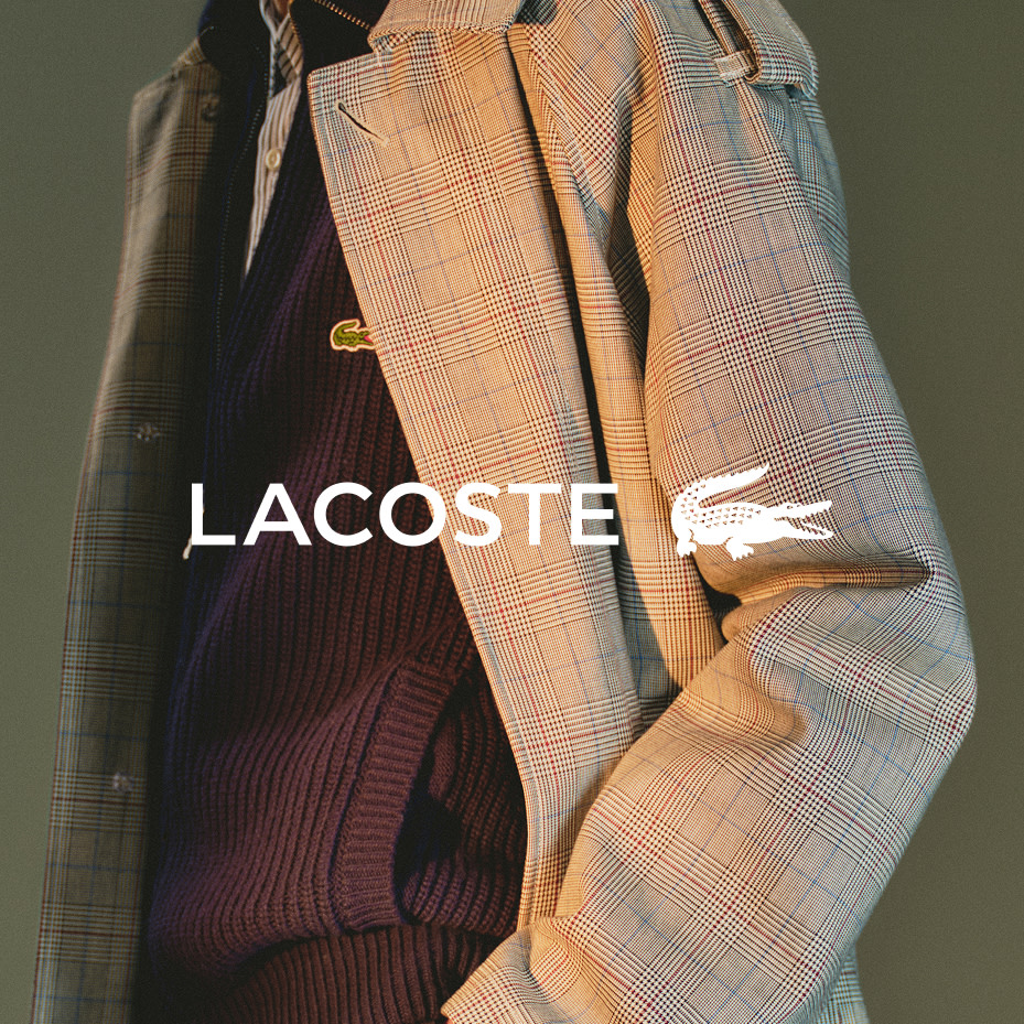 Man wearing checked trench coat and navy sweater by Lacoste