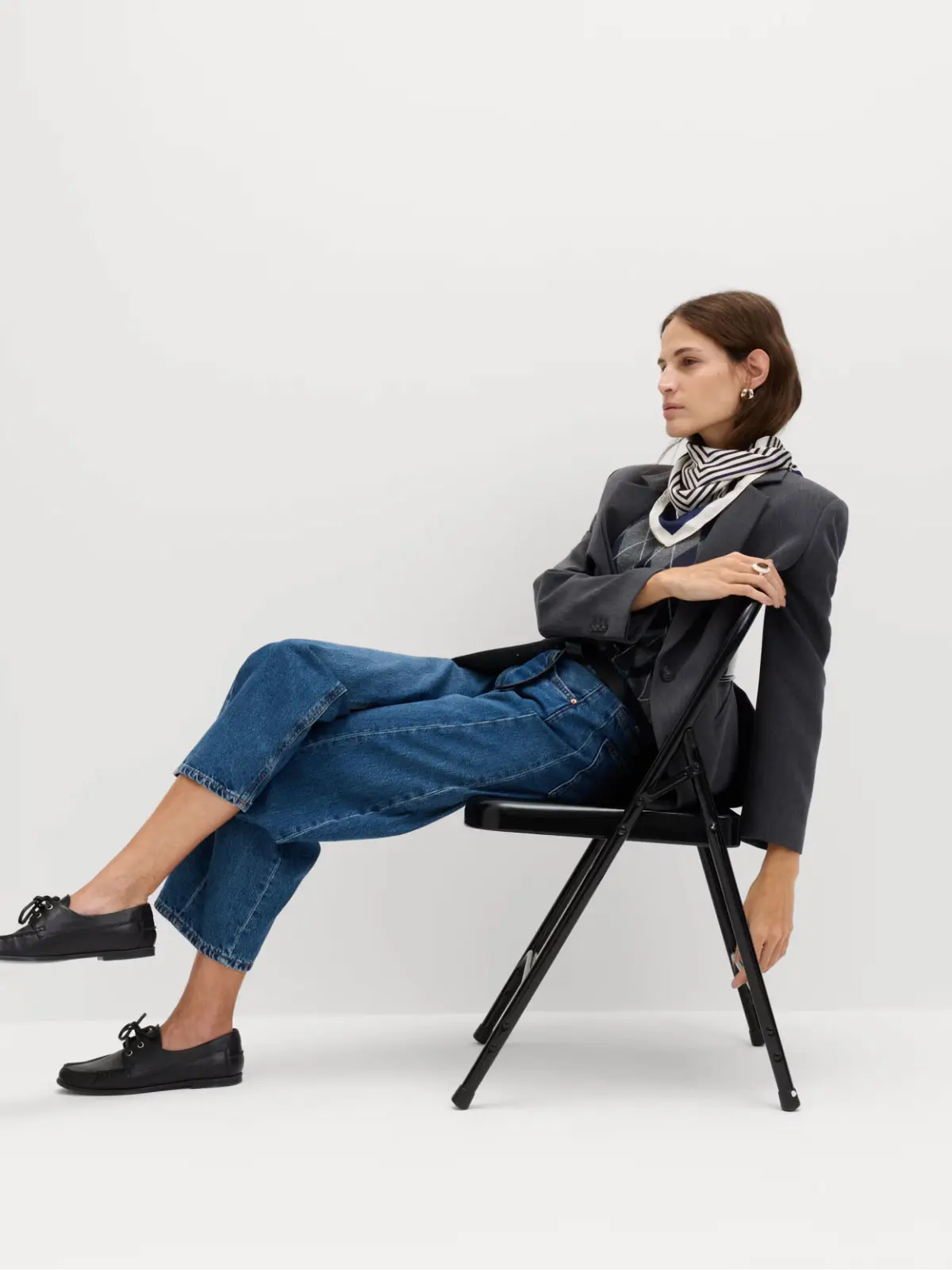 Woman wearing grey blazer, neck scarf, blue jeans and black boat shoes