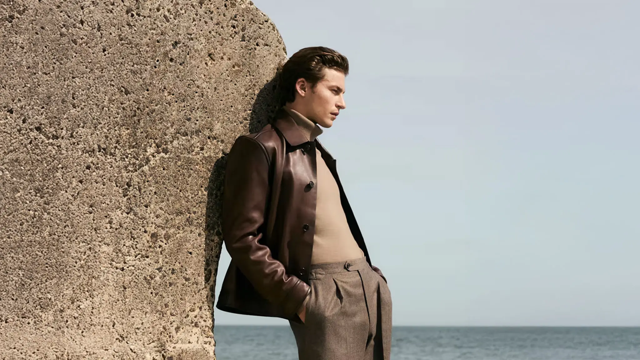 Man wearing a brown leather Harrington jacket with a camel roll-neck jumper and tailored trousers