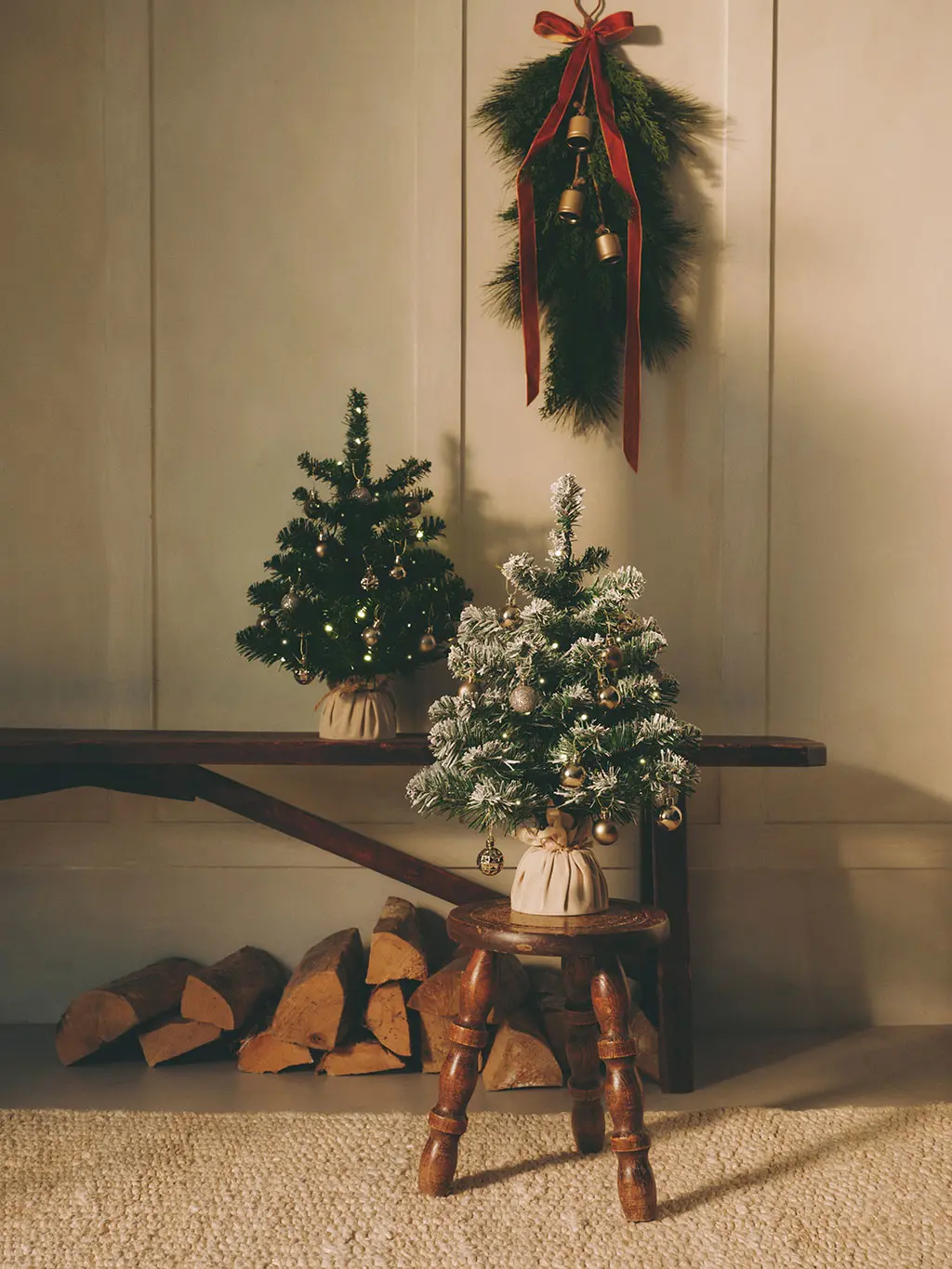 Mini artificial Christmas trees on a wooden bench and stool, decorated with small baubles and lights.