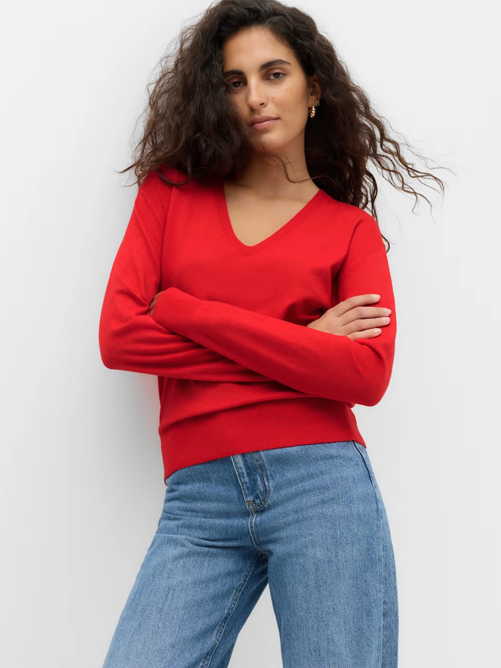 Woman wearing a red V-neck jumper and jeans.