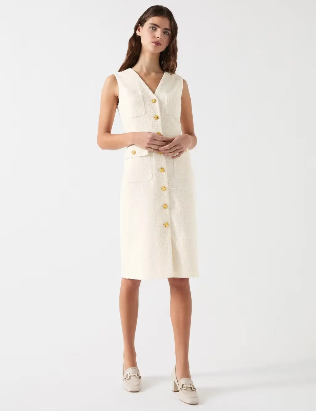 A woman wears a cream sleeveless dress with cream loafers