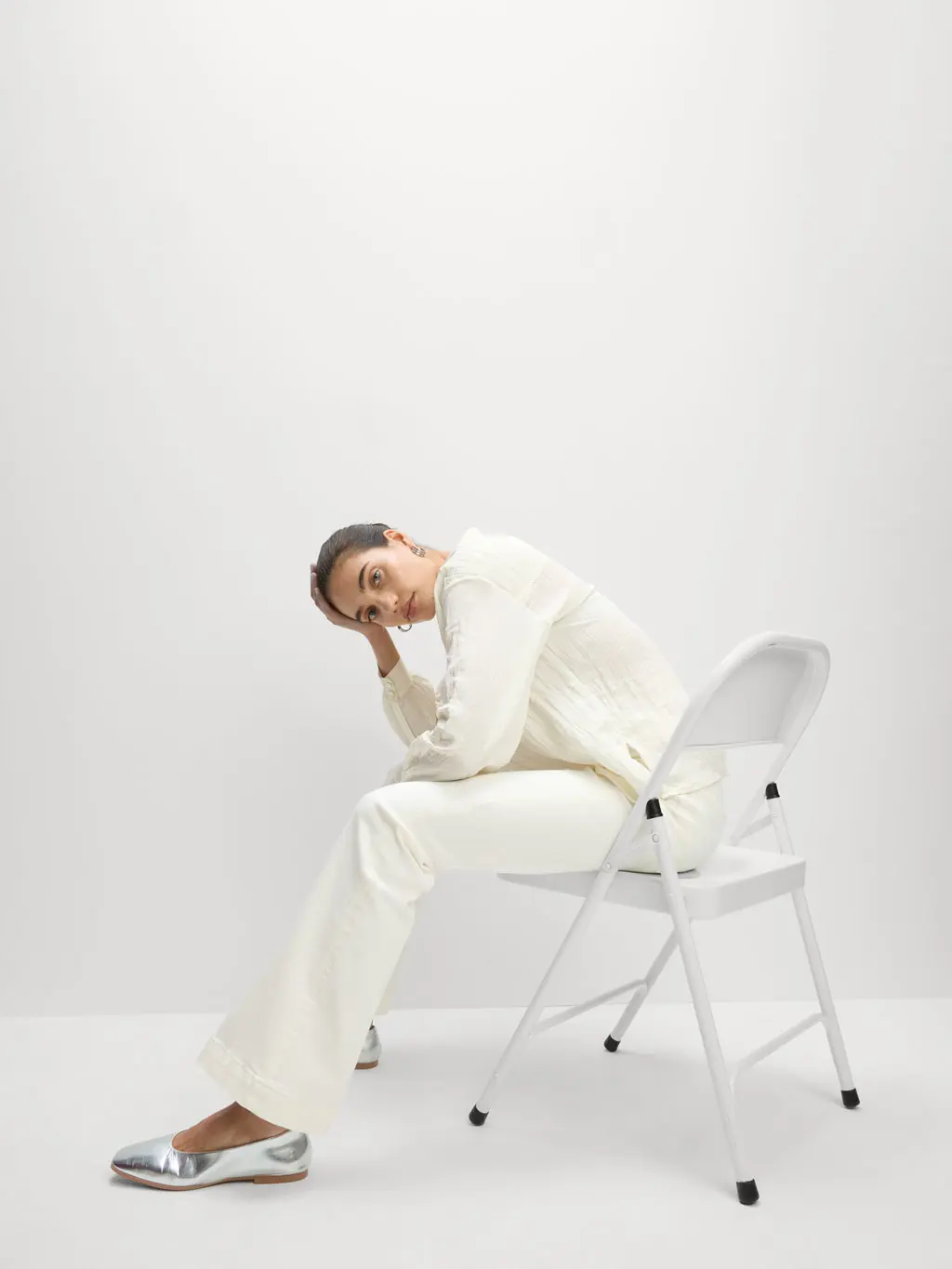Woman wearing white jeans, a white top and silver shoes sat on a chair